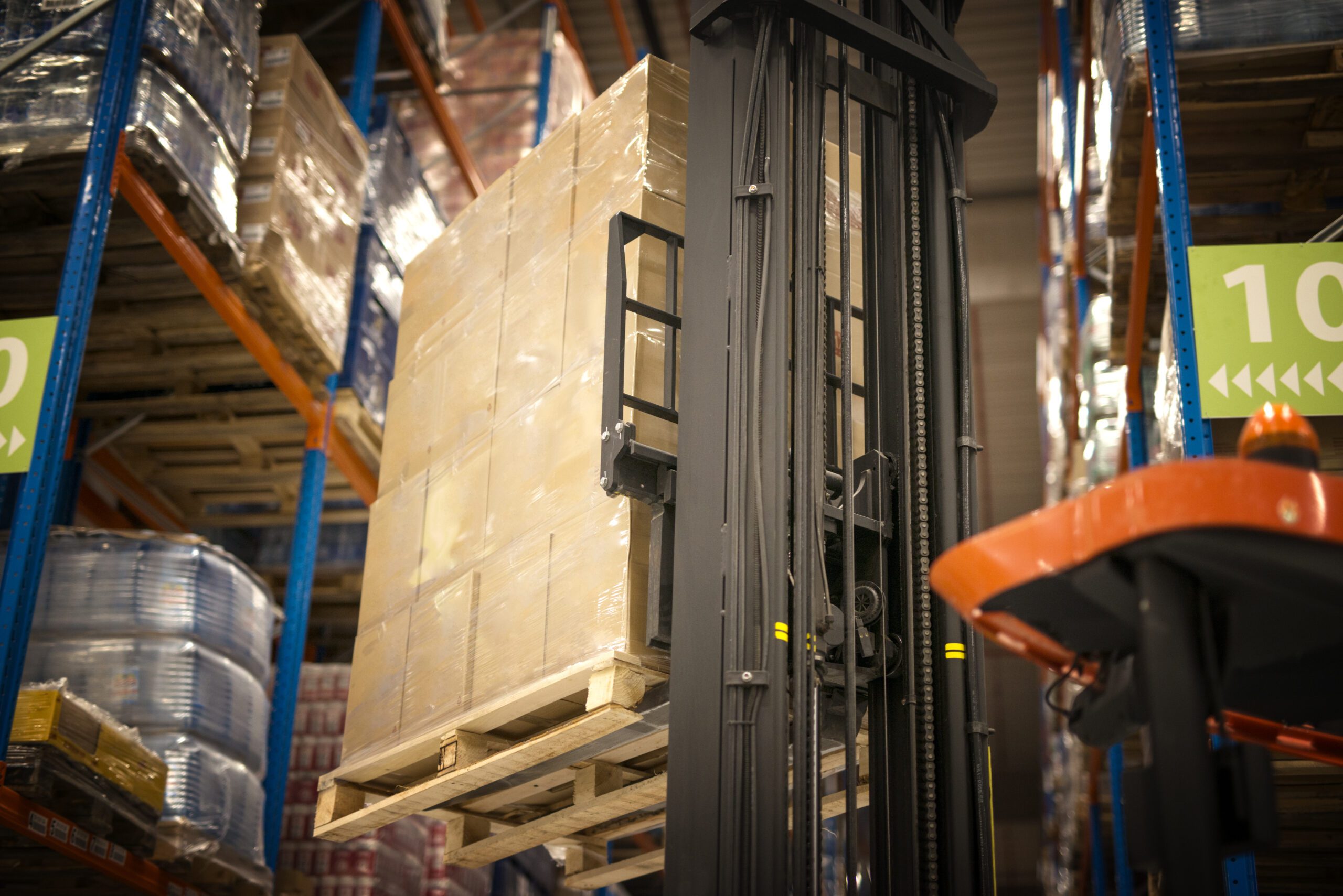 Industrial forklift machine lifting palette full of cardboard boxes and placing them on shelves in distribution warehouse facility